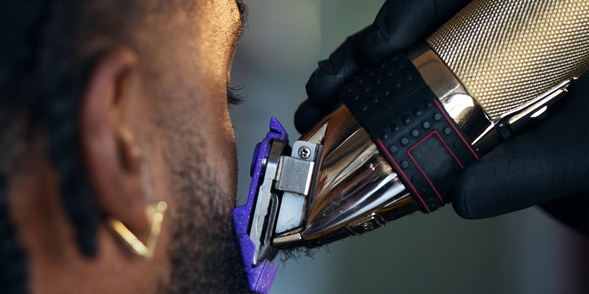 Person using a hair trimmer on another person's head with a blurred background